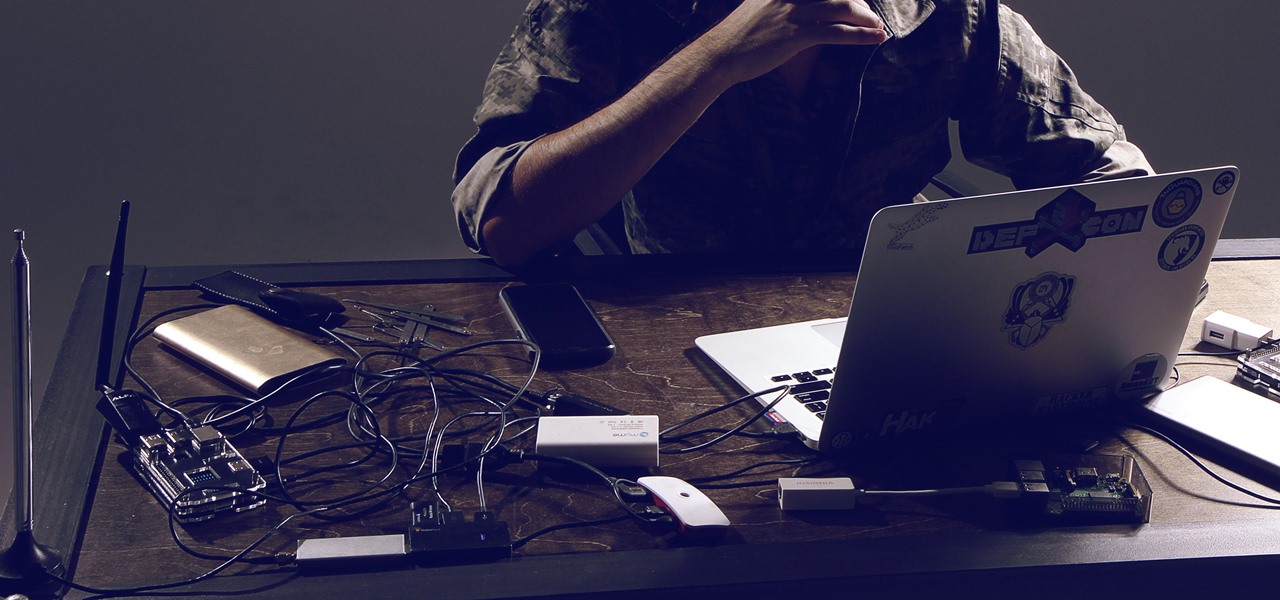 Hacker using a laptop in a dark room surrounded by cables.